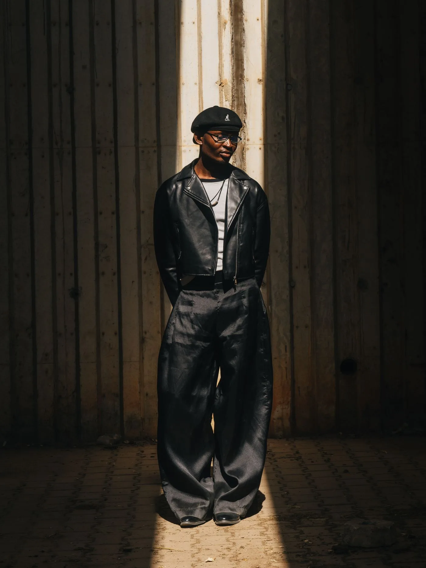 A person in wide-leg trousers and a leather jacket standing in sunlight.