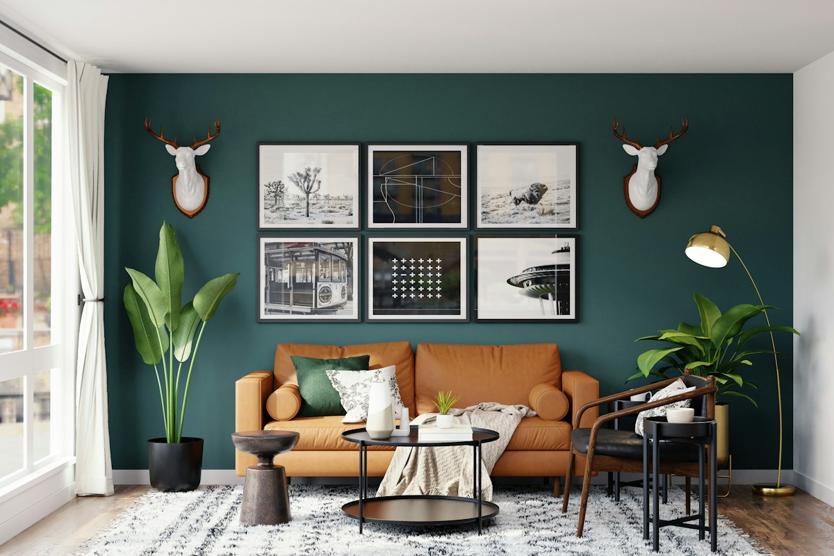 A tan leather sofa against a dark green wall with framed art and deer heads