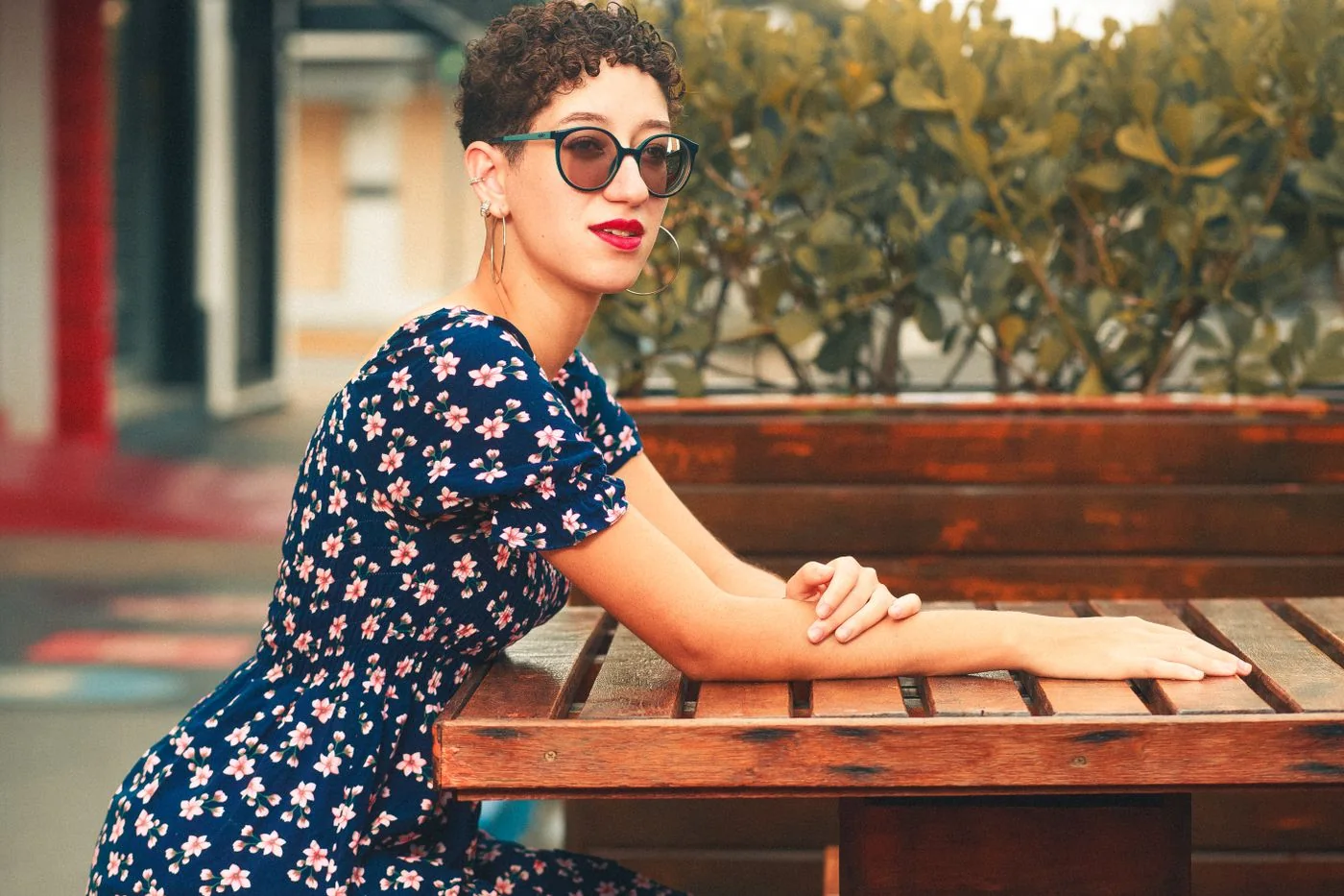 A woman in a floral dress and sunglasses seated at an outdoor cafe table