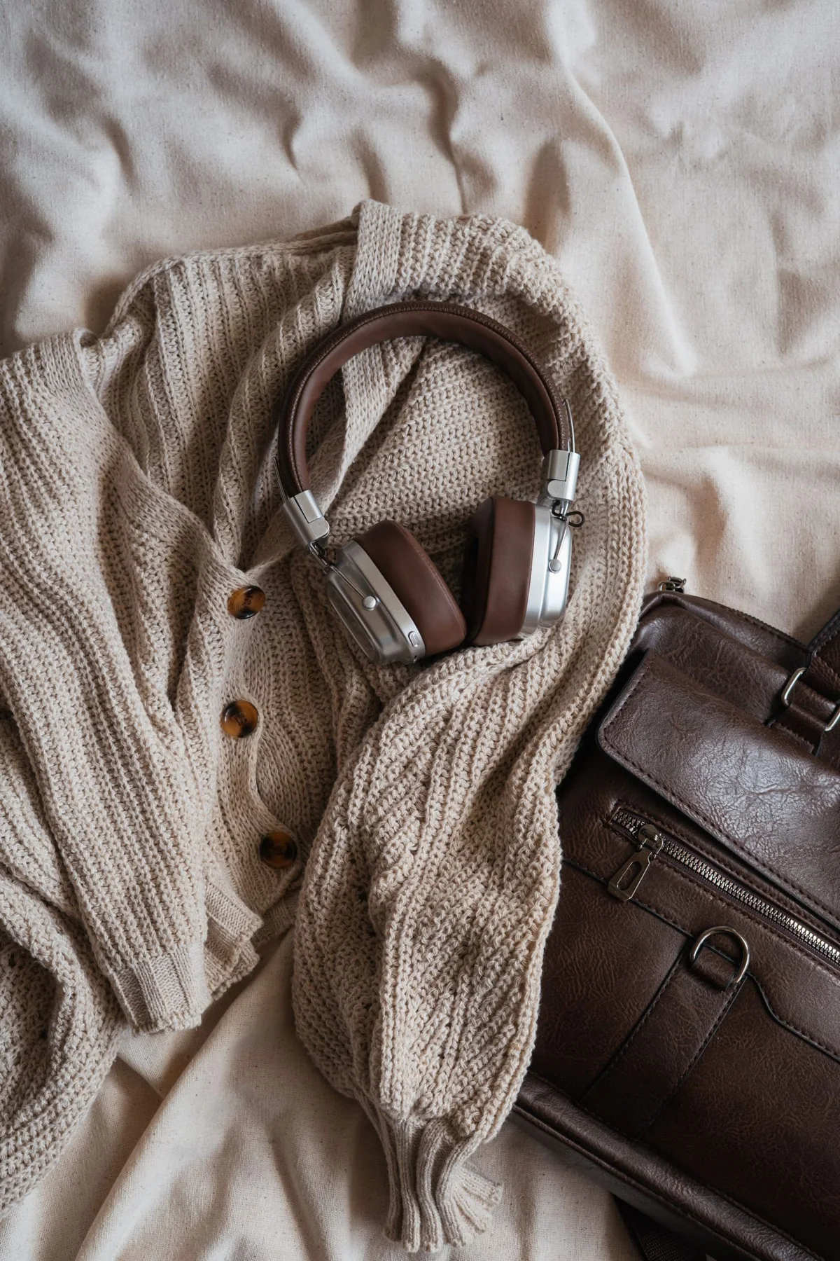 Knitwear, headphones and a dark bag arranged on fabric