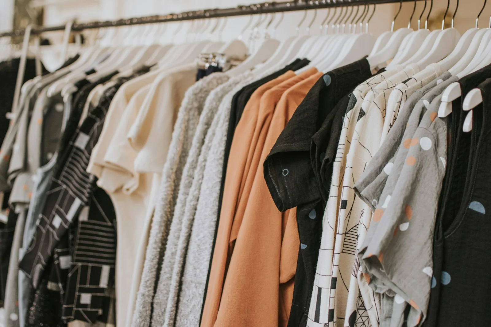 Neutral shirts, patterned garments and an orange piece hang on a clothing rail