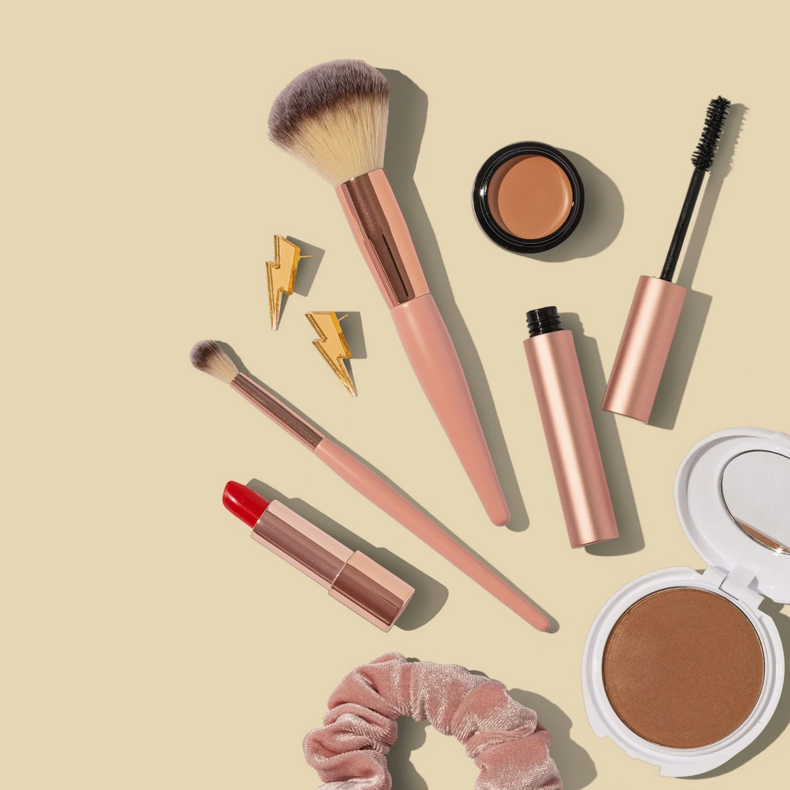 Makeup brushes, lip colours and compacts arranged on a pale background