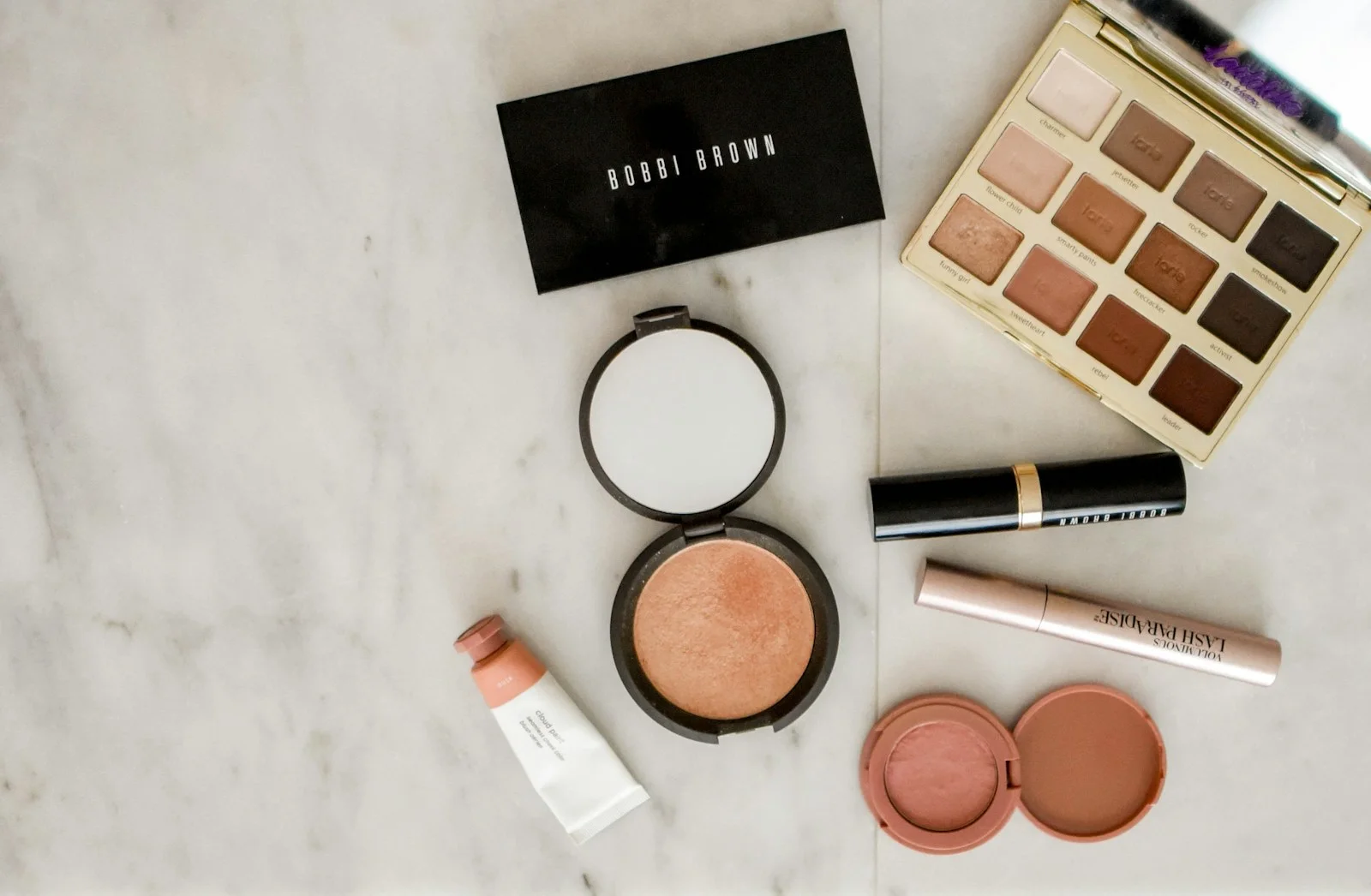 An eyeshadow palette, compacts and makeup brushes on a light surface